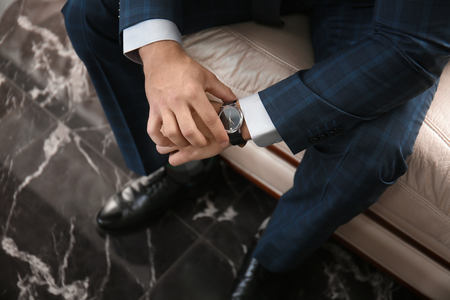 Young man in elegant suit sitting on sofa indoorsの写真素材