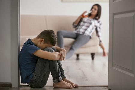 Helpless little boy sitting on floor and his mother drinking alcohol on backgroundの写真素材