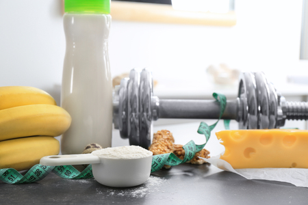 Scoop with protein powder, shake in bottle and products on tableの写真素材