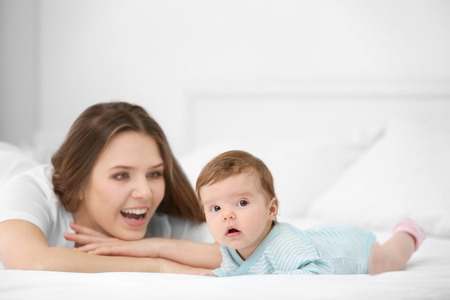 Cute little baby with mother lying on bed at home