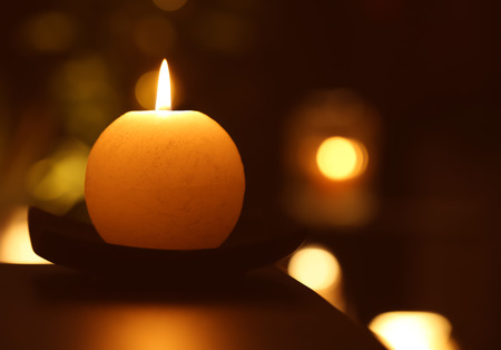 Burning candle in darkness against defocused lightsの写真素材