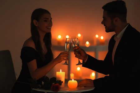 Young couple drinking wine while sitting at table with burning candlesの写真素材
