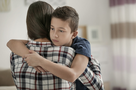 Sad little boy hugging his mother at homeの写真素材