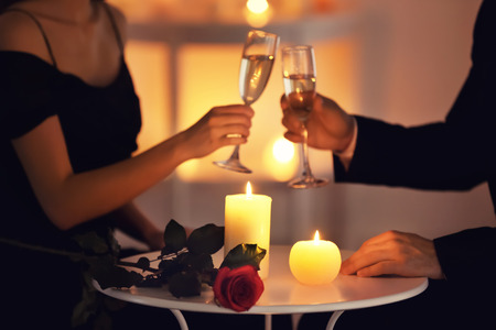 Young couple drinking wine while sitting at table with burning candlesの写真素材