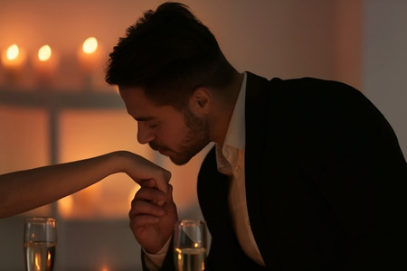Young man kissing his girlfriend's hand on romantic dateの写真素材