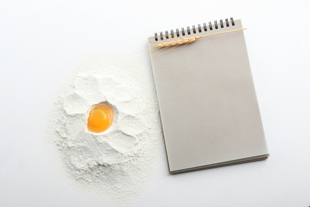 Flour with egg for bread and notebook on white backgroundの写真素材
