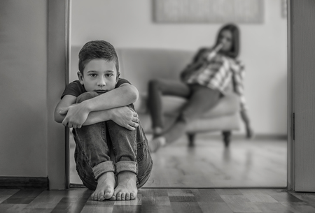 Helpless little boy sitting on floor and his mother drinking alcohol on background, black and white effectの写真素材
