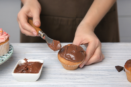 Female baker decorating tasty cupcake with chocolate cream at tableの写真素材