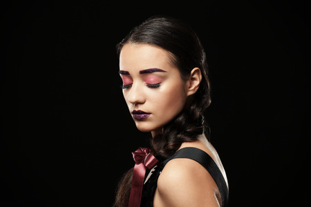 Young woman with dyed eyebrows and creative makeup on black background