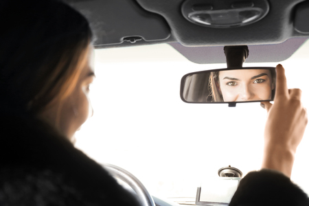 Woman adjusting rear view mirror in carの写真素材