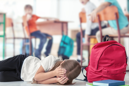 Little girl crying on floor in classroom. Bullying in schoolの写真素材