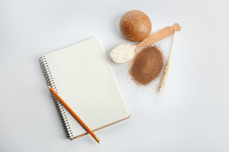 Composition with freshly baked bun, flour and notebook on white backgroundの写真素材