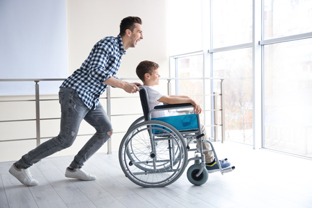 Young man having fun with little boy in wheelchair indoorsの写真素材