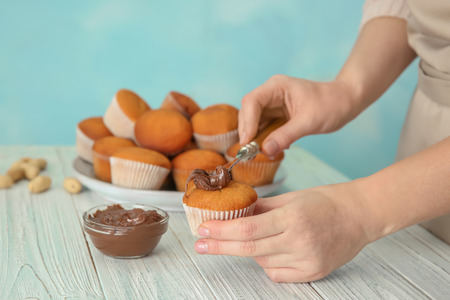 Female baker decorating tasty cupcake with chocolate cream at tableの写真素材