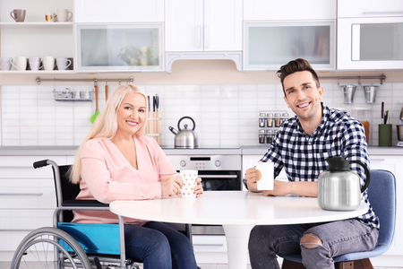 Young man and mature woman in wheelchair drinking tea indoorsの写真素材