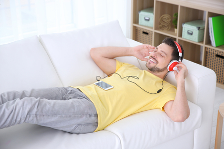 Young man listening to music while relaxing on sofa at homeの写真素材
