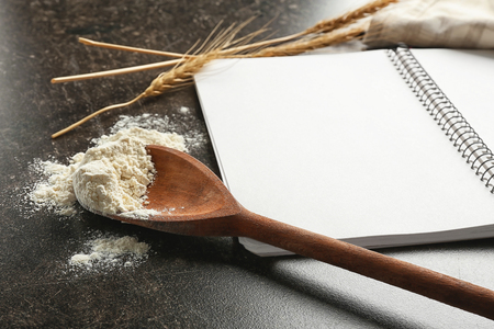 Notebook and wooden spoon with flour for homemade bread on tableの写真素材