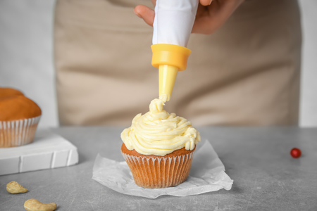 Female baker decorating tasty cupcake with cream at tableの写真素材