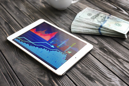 Tablet computer with stock data and money on wooden backgroundの写真素材