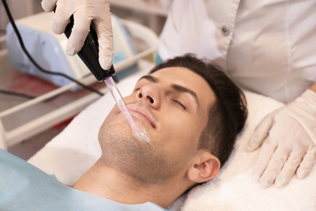 Young man undergoing microcurrent therapy in beauty salon