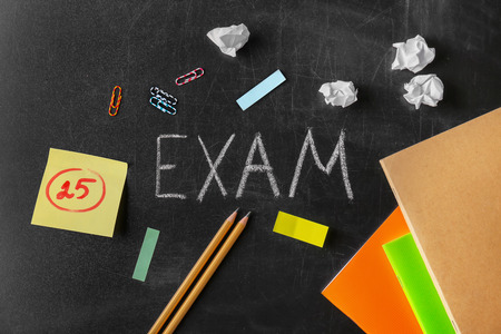 Stationery and word EXAM written on blackboardの写真素材
