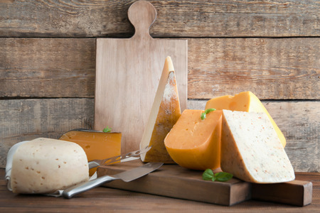 Wooden board with different kinds of delicious cheese on table