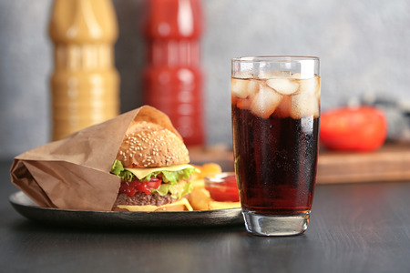 Glass of cold cola with tasty burger on tableの写真素材