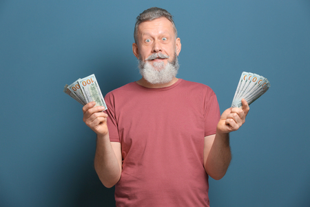 Emotional senior man with lot of dollar banknotes on color backgroundの写真素材