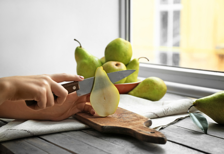 Woman cutting ripe pear on table, closeupの写真素材