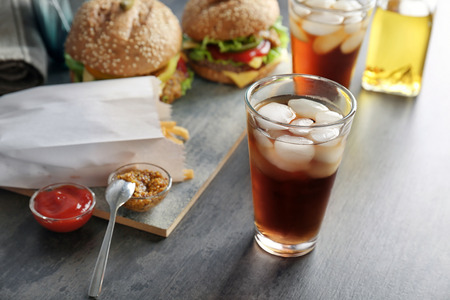Glass of cold cola with tasty burgers on tableの写真素材