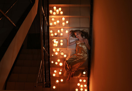 Beautiful young woman lying on stairs with burning candlesの写真素材