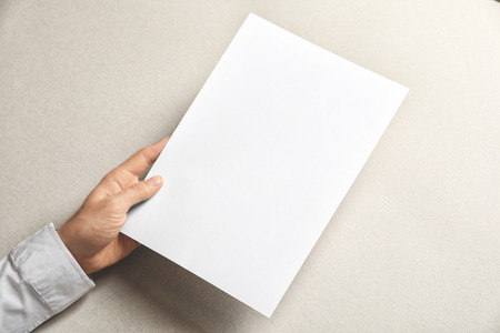 Man holding blank sheet of paper on light background. Mock up for designの写真素材