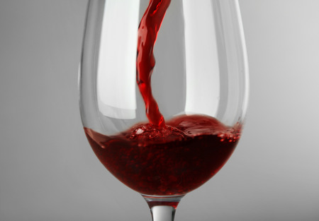 Pouring red wine into glass on gray background