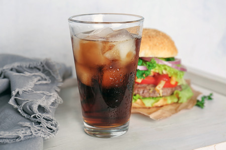 Glass of cold cola with tasty burger on tableの写真素材