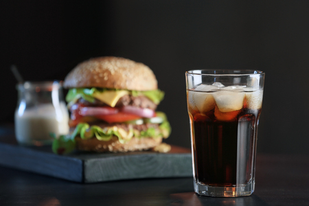Glass of cold cola with tasty burger on dark backgroundの写真素材