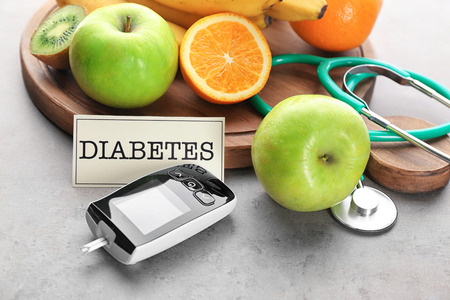 Digital glucometer and fruits on grey background. Diabetes dietの写真素材