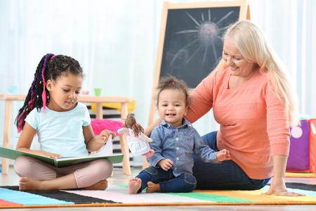 Female mature nanny with little African-American sisters in roomの写真素材