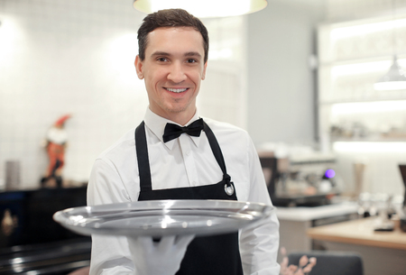 Male waiter holding empty tray indoorsの写真素材