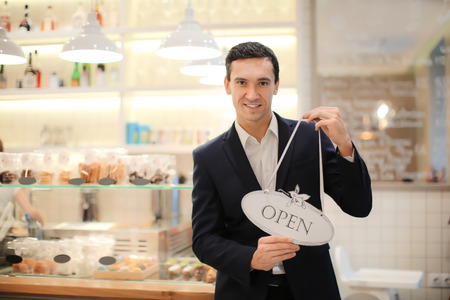 Young man holding Open sign in store. Small business owner portrait