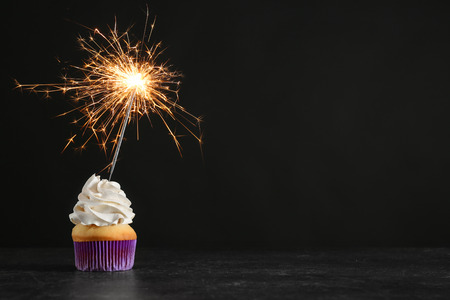Birthday cupcake with sparkler on table against black backgroundの写真素材