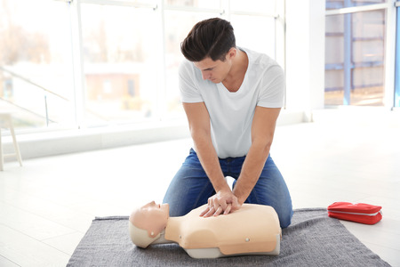 Young man practicing first aid on mannequin indoors