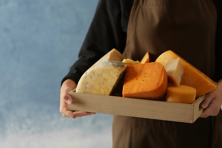 Woman holding wooden tray with variety of cheese on color backgroundの写真素材