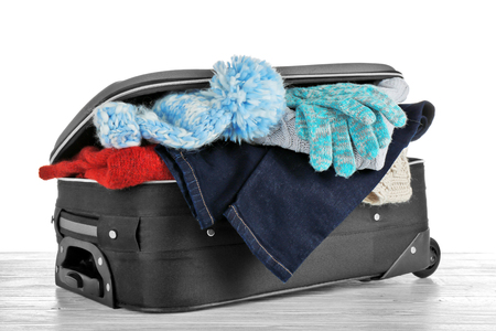 Open suitcase with warm clothes on wooden table against white background. Winter vacation conceptの写真素材