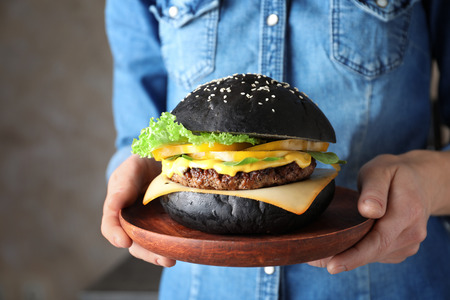 Woman holding plate with tasty black burger, closeupの写真素材