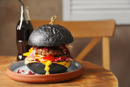 Plate with tasty black burger on tableの写真素材
