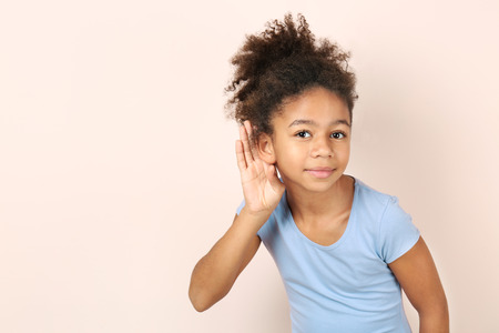 Little African-American girl with hearing problem on light backgroundの写真素材