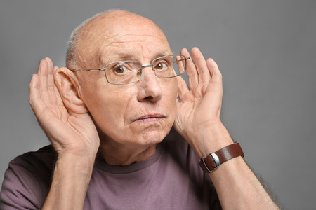 Elderly man with hearing problem on grey backgroundの写真素材