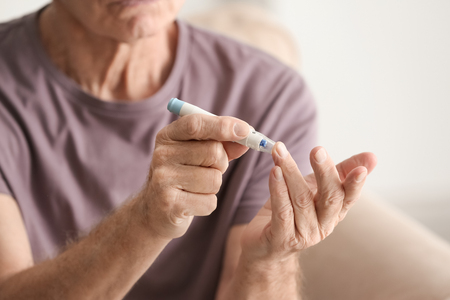 Elderly man with diabetes measuring level of blood sugar at home, closeupの写真素材