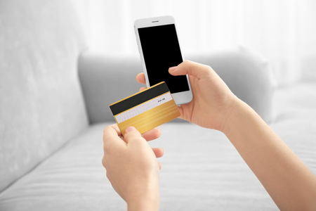 Woman with mobile phone and credit card at home. Internet shopping conceptの写真素材