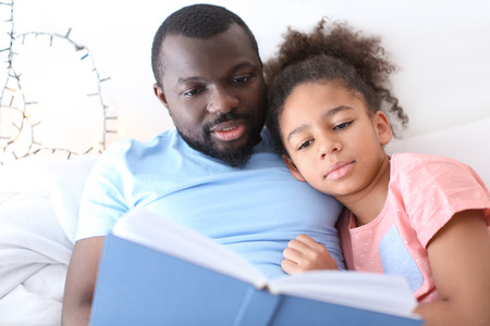 African American man reading bedtime story to his daughter in bedの写真素材